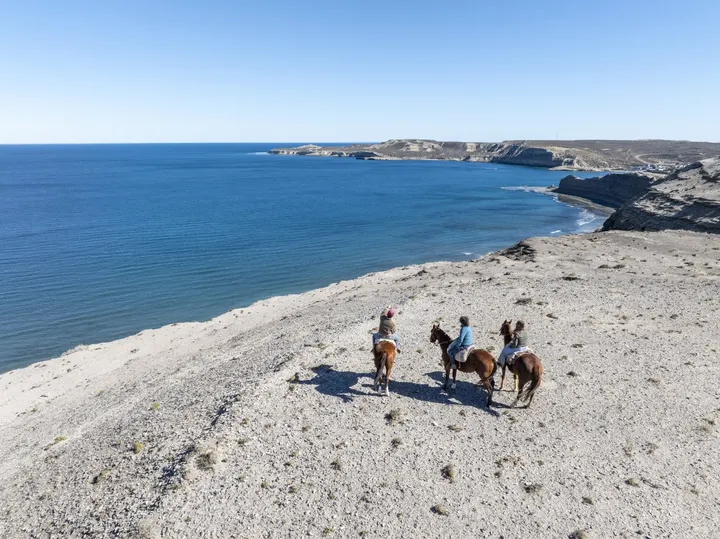 Vista aérea de tres jinetes sobre los acantilados y el mar azul