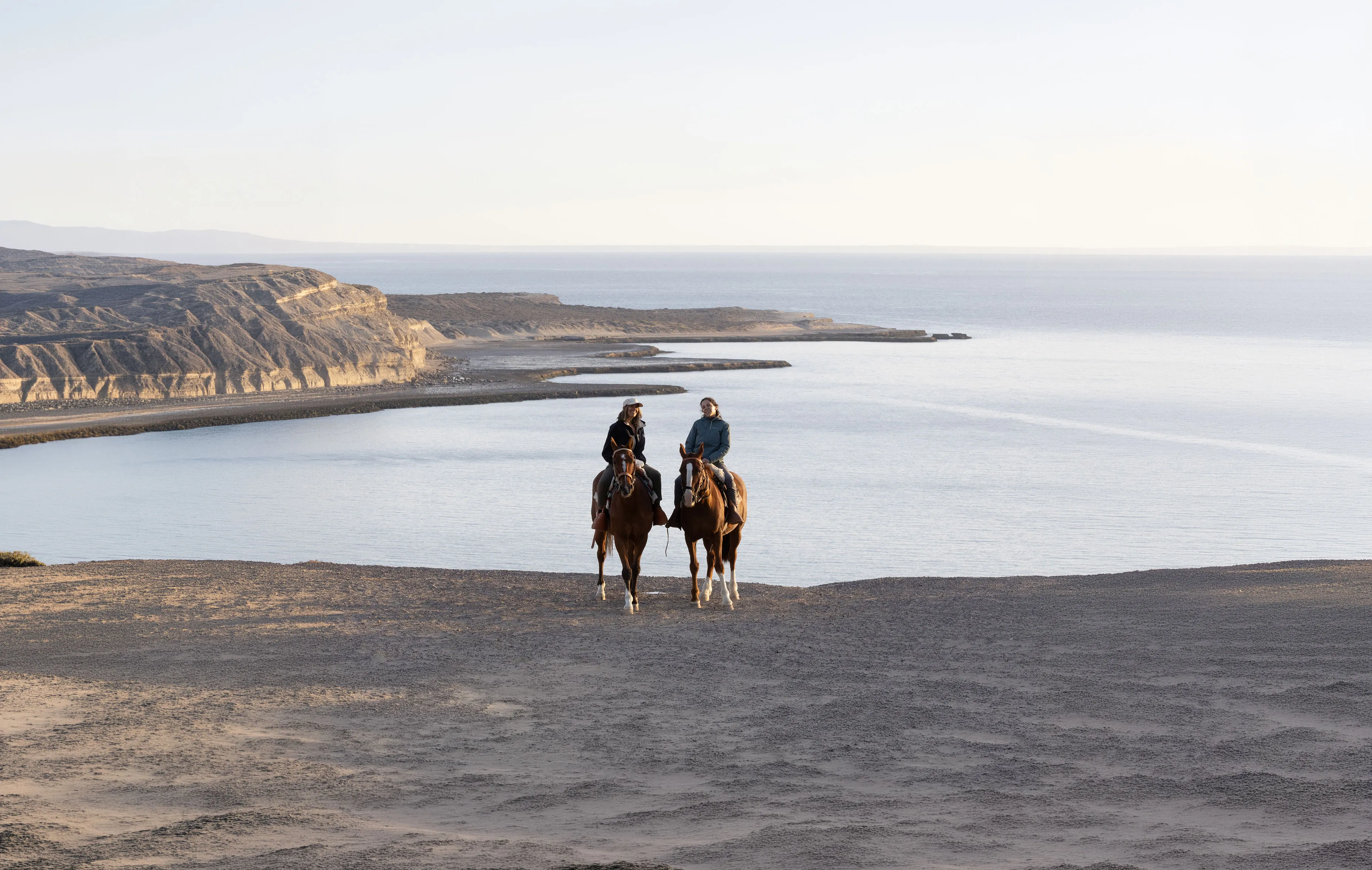 Dos jinetes a caballo frente a la costa de Península Valdés al atardecer